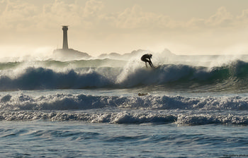 Surfing longships This landscape photograph captures surfing activity at Longships off the coast near Sennen Cove in the United Kingdom, during a bright autumn afternoon. In the foreground, powerful sea waves are depicted with a surfer riding atop the crest, emphasizing the dynamic nature of the scene. The iconic Longships Lighthouse, a well-known landmark, is visible in the distance, standing on a rocky outcrop surrounded by the ocean. The light mist and clouds in the sky enhance the natural atmosphere of the coast, while the overall composition showcases both the exhilarating energy of the waves and the enduring presence of the lighthouse. This image highlights the natural beauty of Sennen Cove, the power of the sea, and the popular sport of surfing in this part of the United Kingdom.